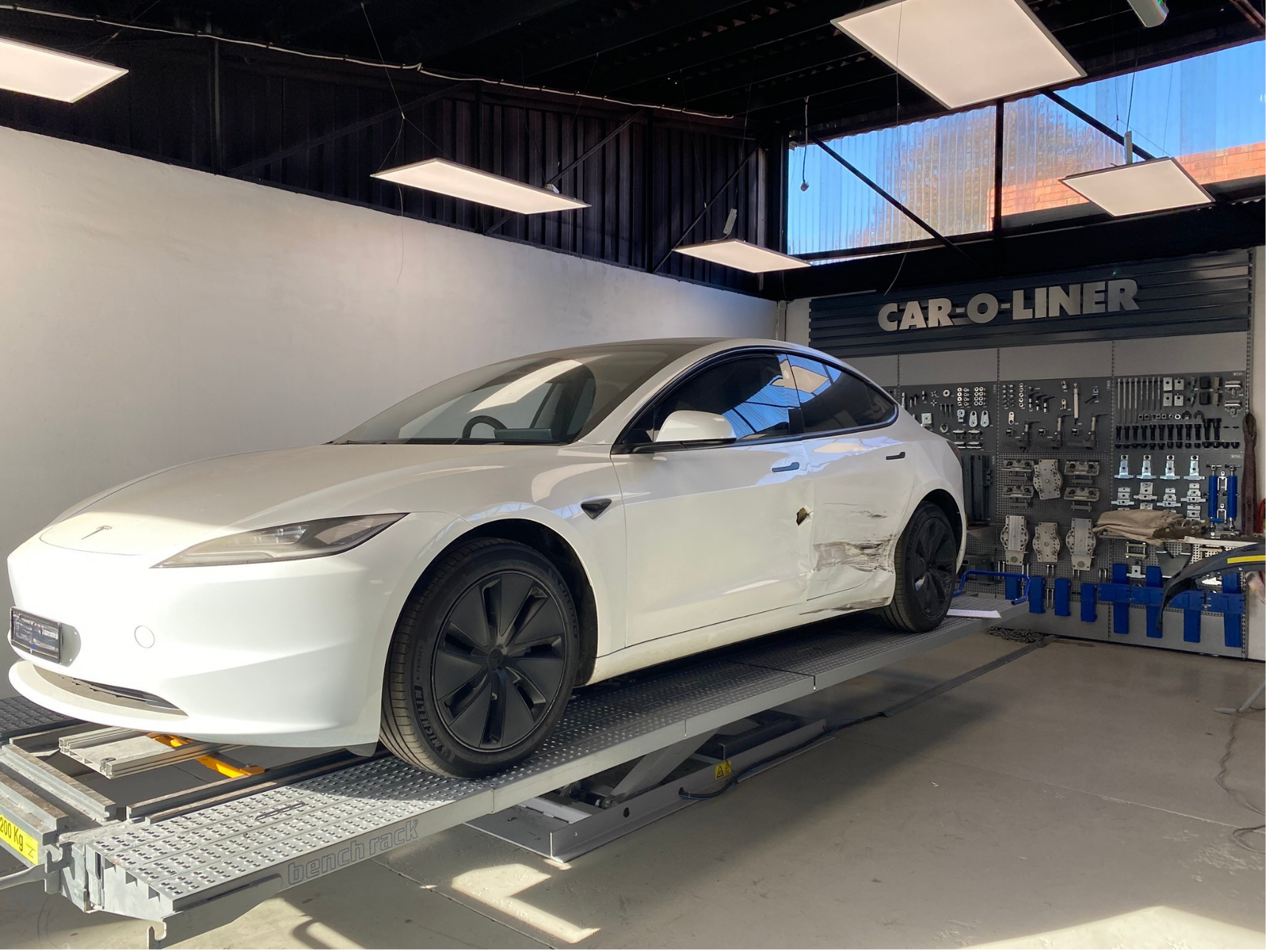 White Tesla with accident damage inside Box Hill Accident Repair Centre workshop, beside Car-O-Liner equipment